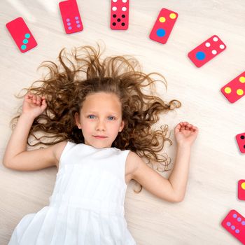 Portrait of cute little girl laying on floor with domino pieces.