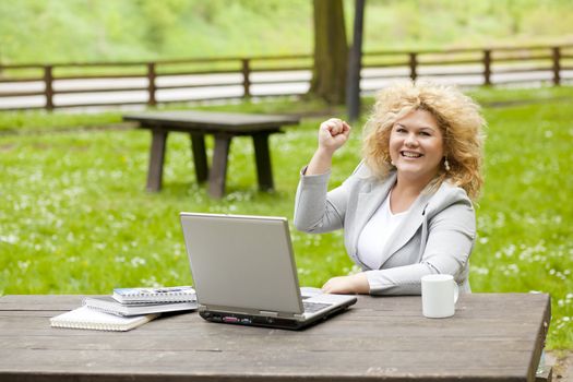 Young woman using laptop in park, fist hand up