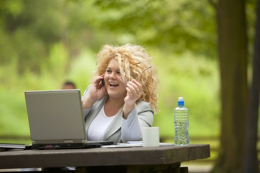 Young woman using phone and laptop in park