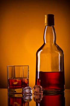 whiskey bottle, ice and glass, orange background