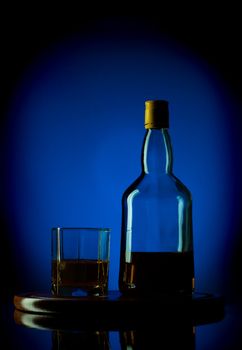 whiskey bottle and glass on wooden tray, blue background