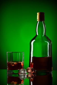 whiskey bottle, ice and glass, green background