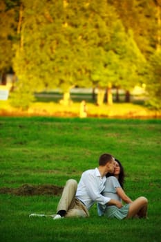young couple sitting on park lawn and embrace