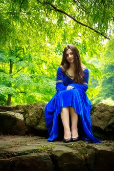 medieval girl in blue dress sitting on stone stage