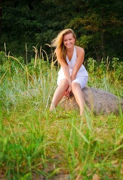 pretty woman in white dress sitting on big stone