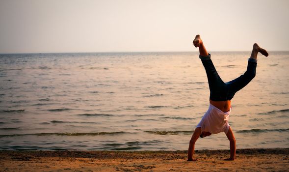 man doing handstand on sunset beach