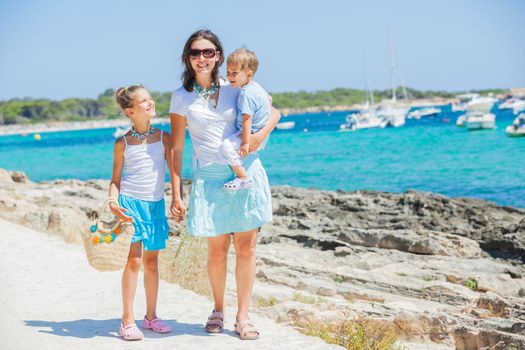 Young beautiful family of three walking along tropical beach