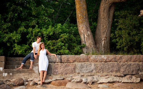 young couple stand next stonewall in forest