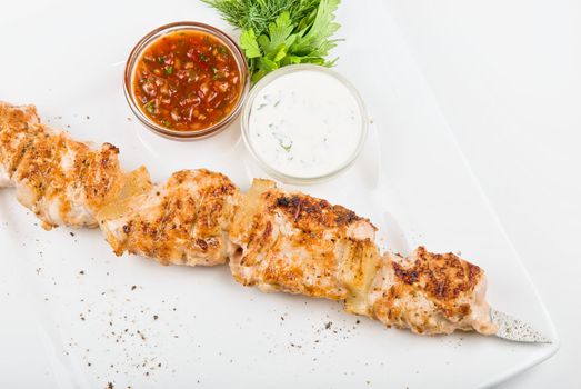 Grilled chicken kebab with sauce and greens on white plate 