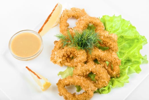 Deep-fried squid with salad leaves, sauce, green and lemon on a white background