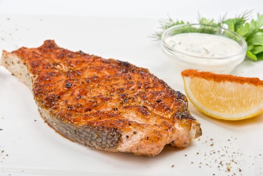 Grilled fish with sauce, lemon and greens on white plate 
