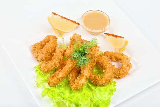 Deep-fried squid with salad leaves, sauce, green and lemon on a white background