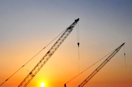 Industrial construction cranes and building silhouettes over sun at sunrise.