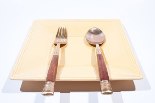 Orange square shaped plate with spoon and fork is placed on a white background.