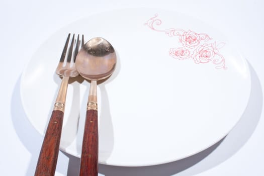 Round white plate with spoon and fork is placed on a white background.