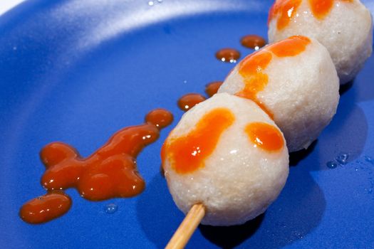 Wet ball grill skewers on the plate topped with spicy sauce placed on a plate. A white background. Blue needle plate.