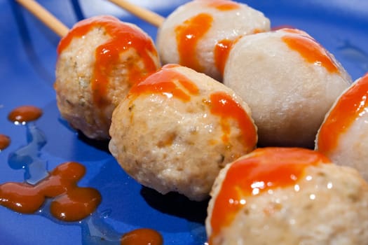 Wet ball grill skewers on the plate topped with spicy sauce placed on a plate. A white background. Blue needle plate.