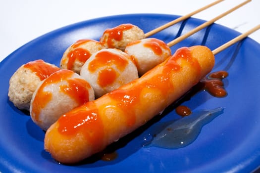 Wet ball grill skewers on the plate topped with spicy sauce placed on a plate. A white background. Blue needle plate.