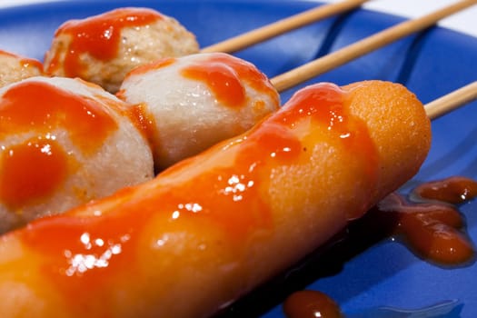 Wet ball grill skewers on the plate topped with spicy sauce placed on a plate. A white background. Blue needle plate.