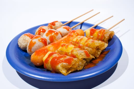 Wet ball grill skewers on the plate topped with spicy sauce placed on a plate. A white background. Blue needle plate.