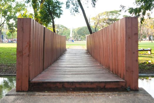 Wooden bridge across the river in the park. Next to the lawn.