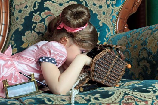 A girl plays with her ​​mother's jewelry lying on the couch.