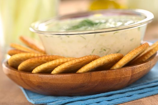 Salty crackers with a tzatziki dip made of yoghurt, cucumber, garlic, olive oil and dill (Selective Focus, Focus on the front of the two crackers in the middle)