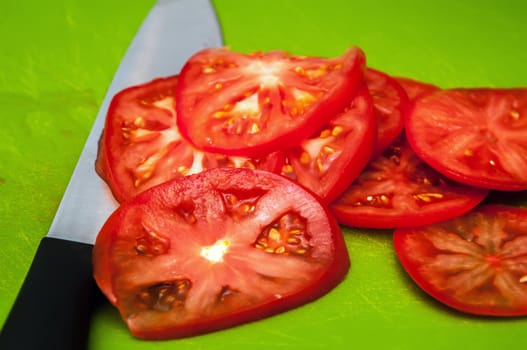 Red tomato slices and knife on green chopping board