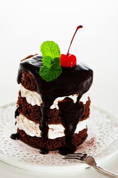 A small chocolate cake with 2 layer white cream, cherry and mint  on top on a white background as a studio shot