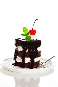 A small chocolate cake with 2 layer white cream, cherry and mint  on top on a white background as a studio shot