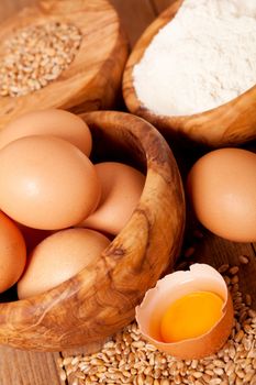 eggs with wheat grain and flour, on wooden background