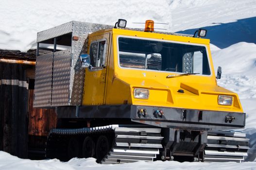 Old snow groomer / snowcat functioning as transporter standing nearby cottage