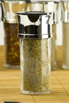 oregano in a glass jar on different spices background over wooden mat