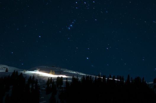 Night panorama of Montafon, Austria with great starry sky and snow groomer preparing the piste