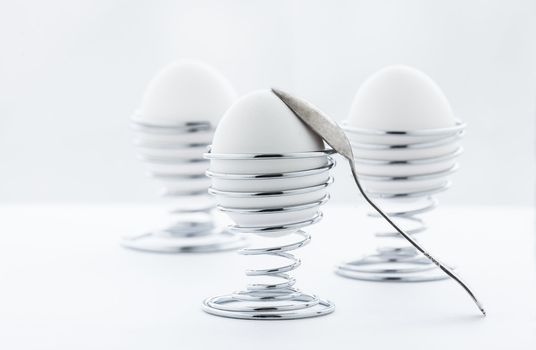 Three eggs in metal stands with a spoon