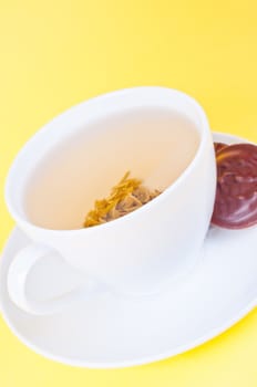 Cup of green tea on the saucer and cookies on yellow background