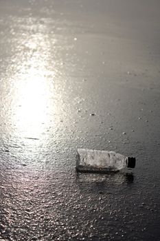 A plastic bottle lying in the beach sands after being thrown out by the sea waves.