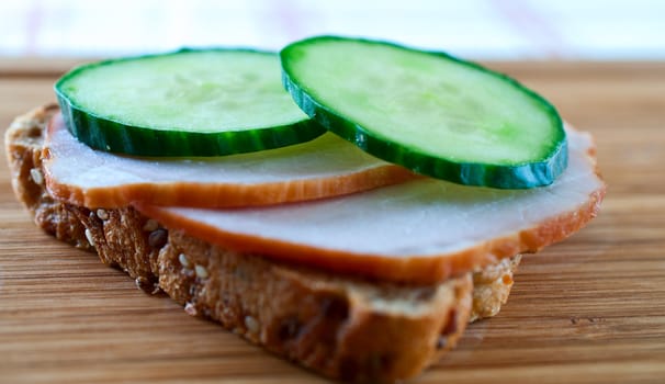 Sandwich with ham and cucumber on a wooden board close up