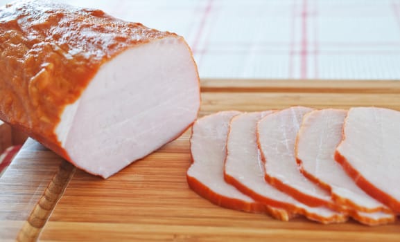 Ham cut into slices on a wooden board close up