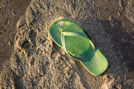 A green flipflop lying in the beach sands.