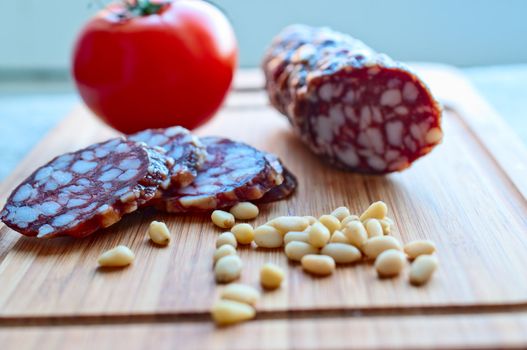 Sausage, tomato, pine nuts on  wooden board close up