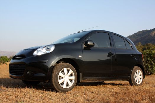 A black hatchback car parked in the countryside grass.