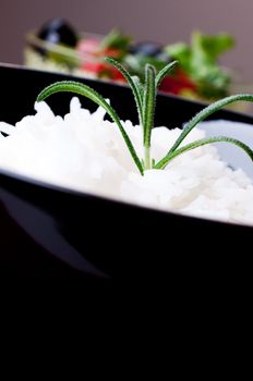 White rice in black bowl on salad background