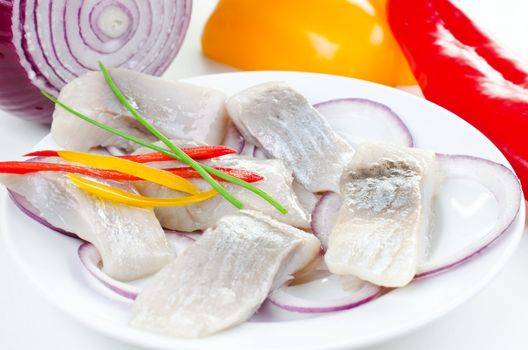 Herring bites on a plate with vegetables red yellow pepper and onion