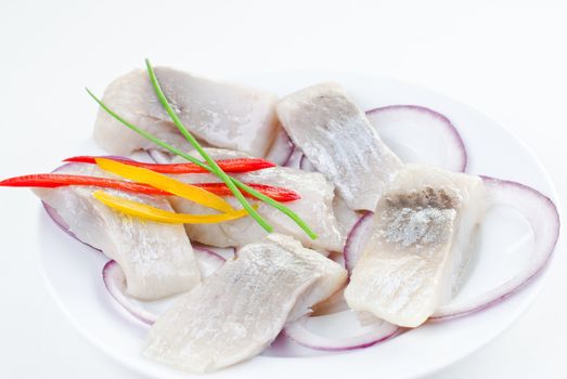 Marinated atlantic herring bites with vegetables on white porceline plate