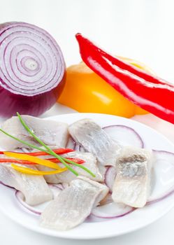 Marinated herring bites on a plate with onion and red and yellow pepper