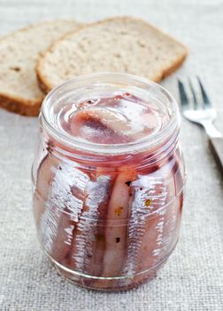 Atlantic marinated herring in glass jar with bread and fork