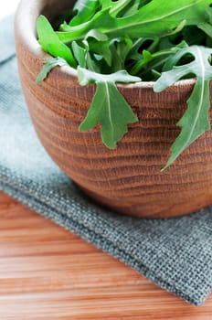 Wooden bowl with rucola on cloth close up