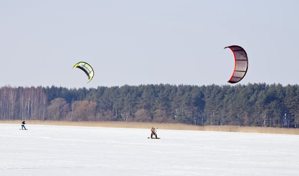 Kiteboarding with snowboards on frozen lake in winter. Active and modern people leisure.