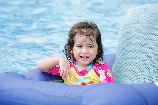 Baby girl having fun on a blue float into a tropical swimming pool